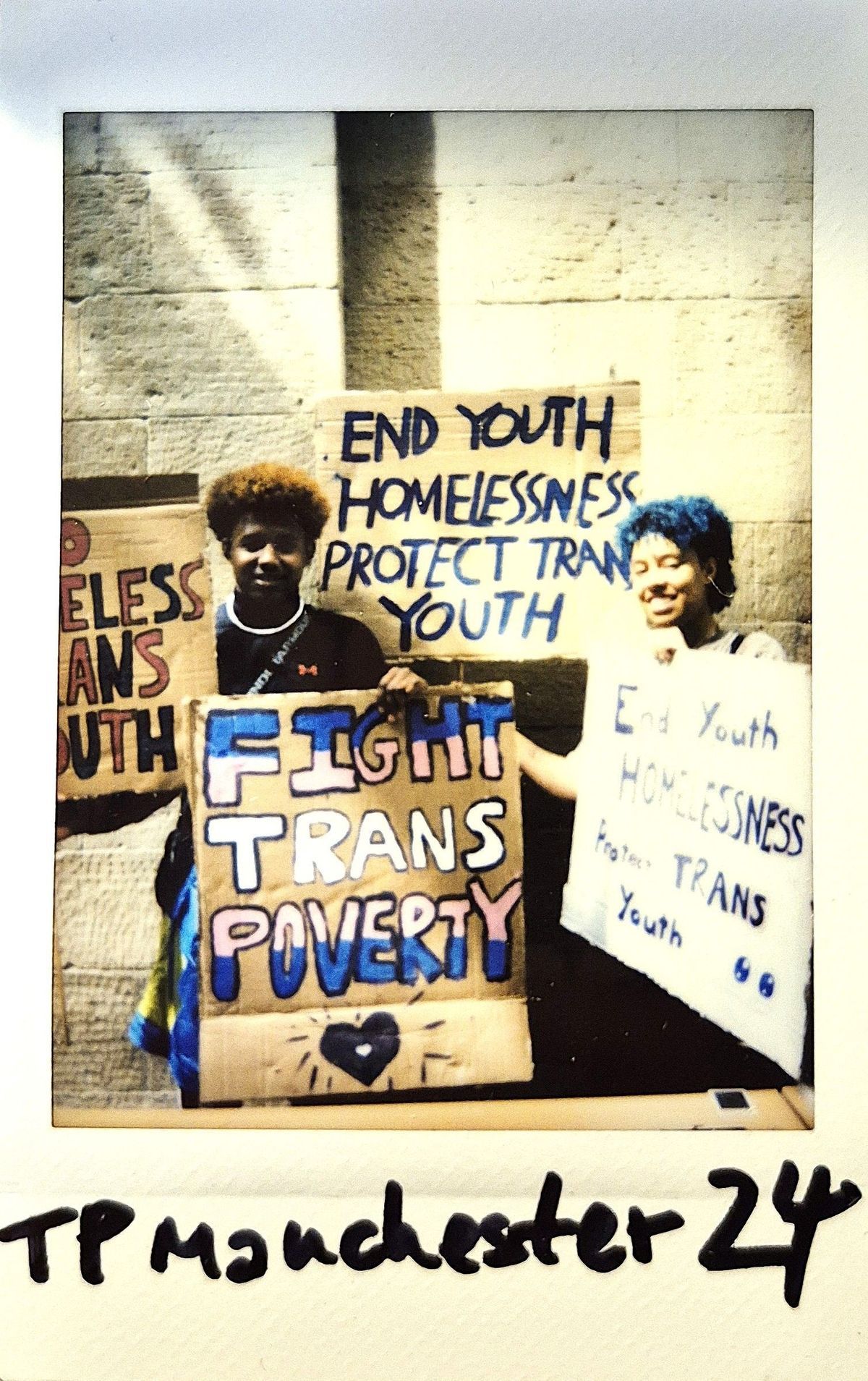 Two people hold signs advocating for ending youth homelessness and supporting trans youth.