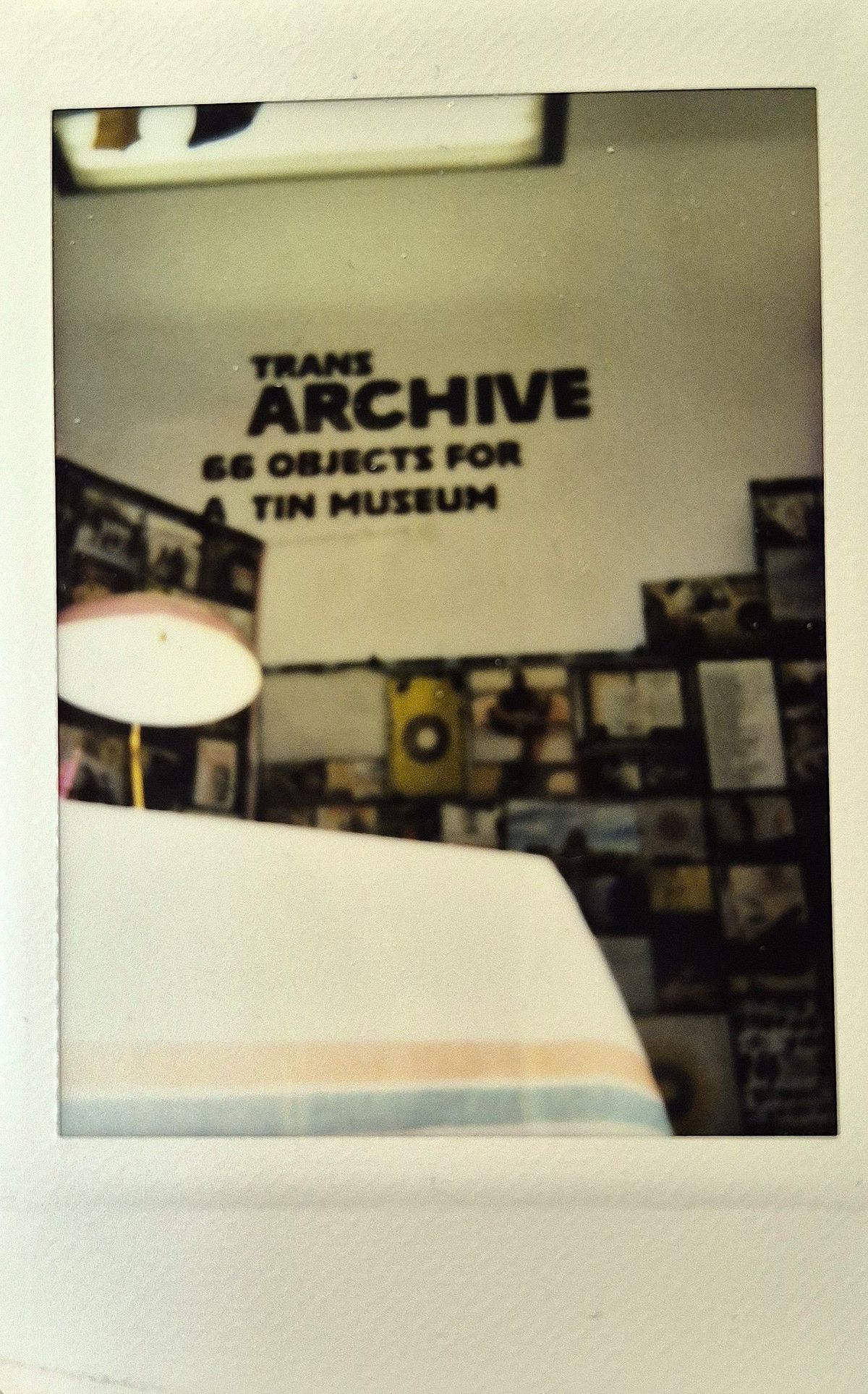 A room displays a sign reading "TRANS ARCHIVE: 66 Objects For A Tin Museum".
