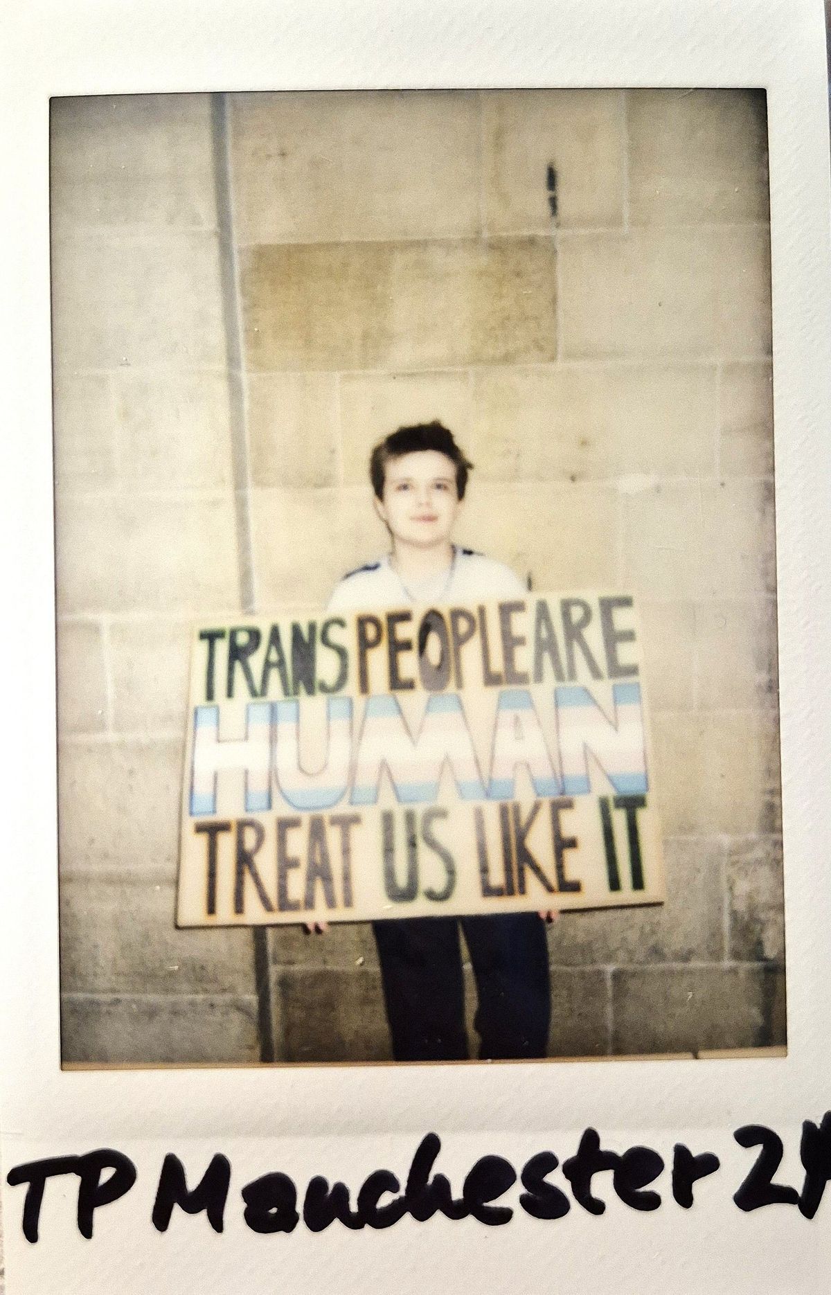 A person holds a sign that reads "Trans People Are Human, Treat Us Like It."