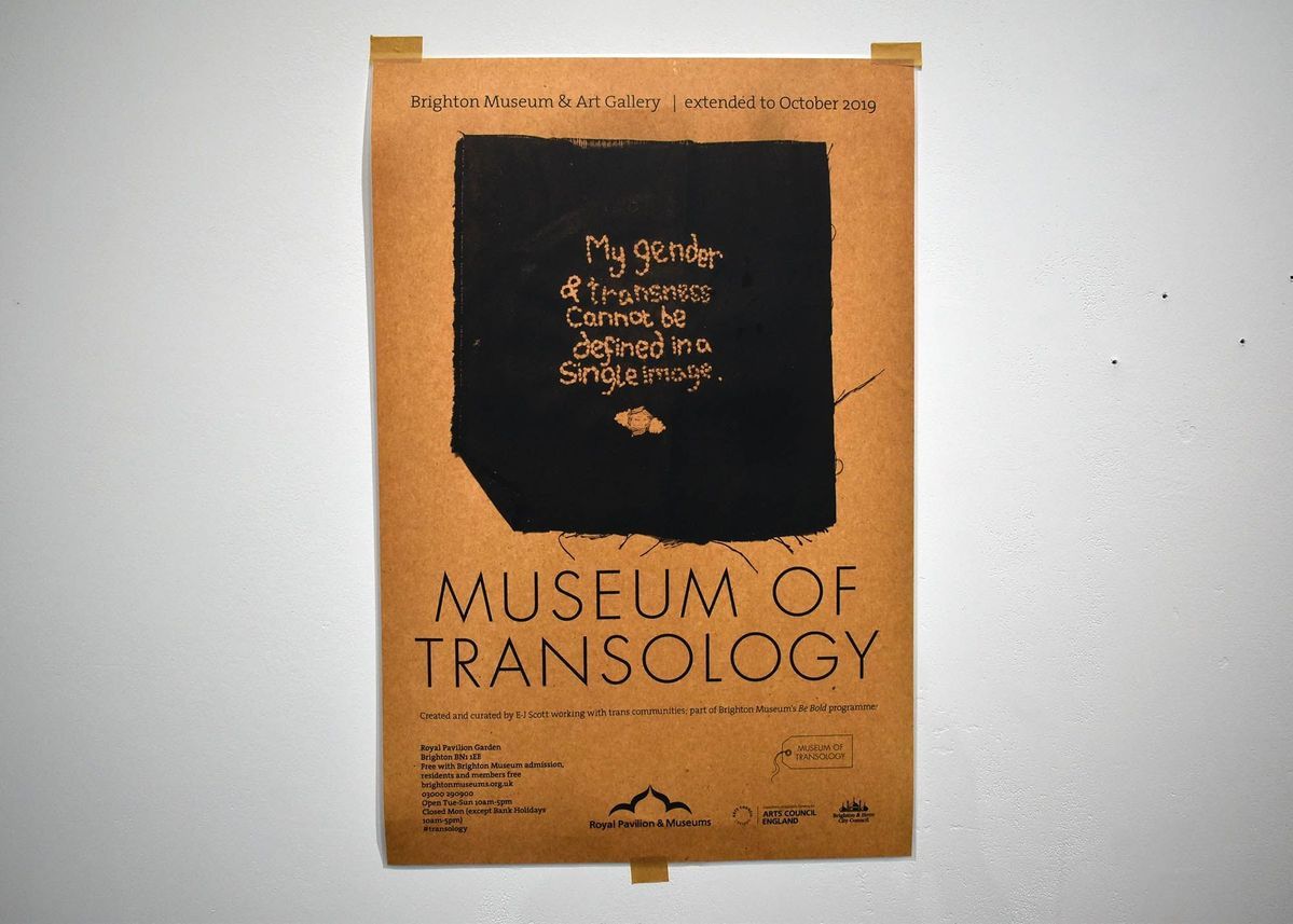 Beige poster reading "Brighton Museum & Art Gallery / extended to October 2019" [image of black fabric with embroidery reading "My gender & transness cannot be defined in a single image."] "MUSEUM OF TRANSOLOGY". under this there are some credits listed along with logos and other information.