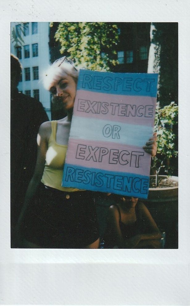 A person holds a sign with the message, “Respect existence or expect resistance” outdoors.