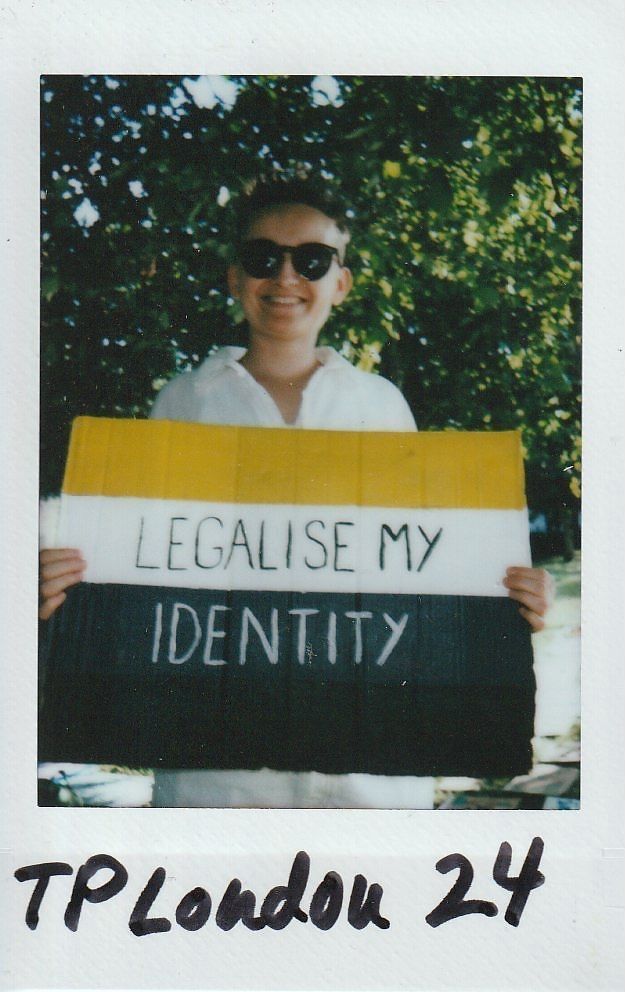 A person holding a sign with "LEGALISE MY IDENTITY" stands outdoors, wearing sunglasses.