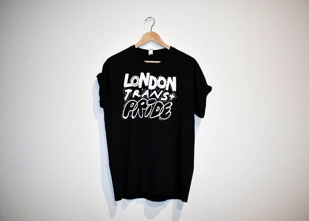 A black T-shirt with the text "LONDON TRANS+ PRIDE" in white on the front. On a wooden hanger.