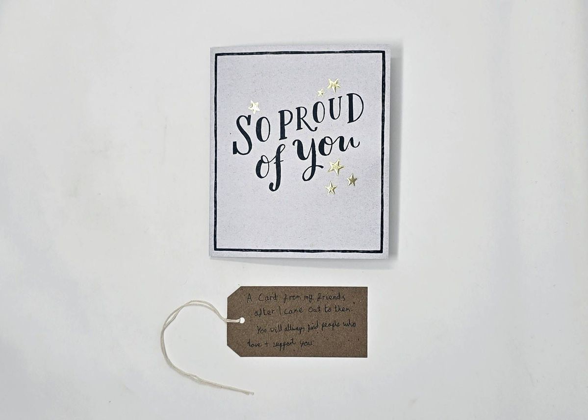 A white card, bordered in black with the text "SO PROUD of you" surrounded with gold stars. With a brown, handwritten luggage tag.