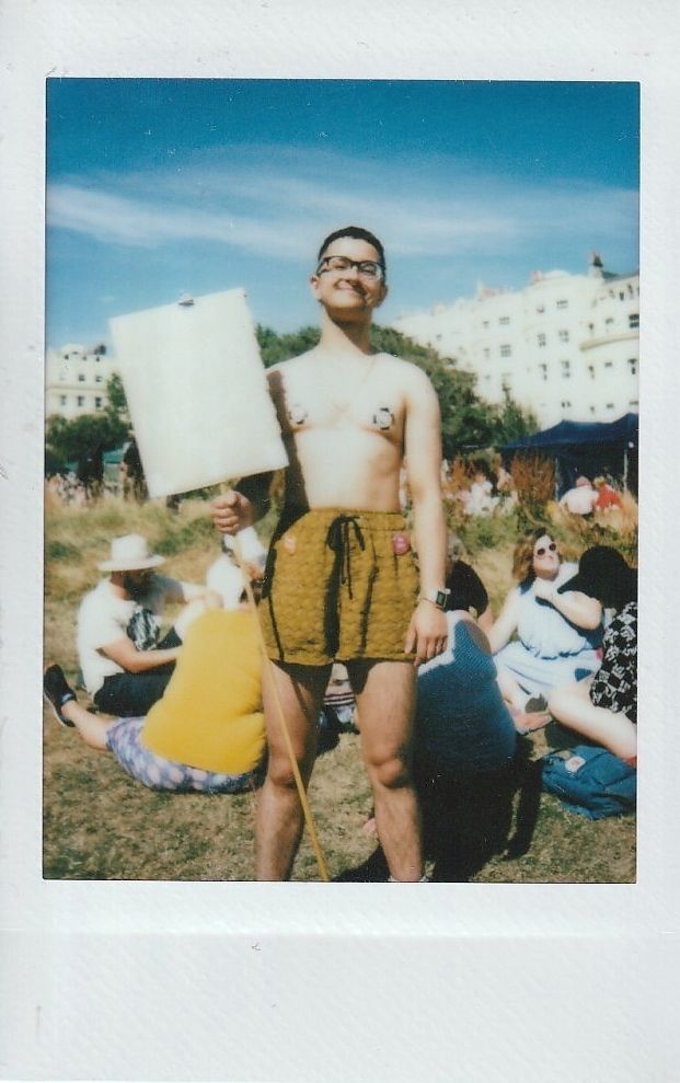 A person is holding a blank sign and standing confidently in a sunny outdoor gathering.