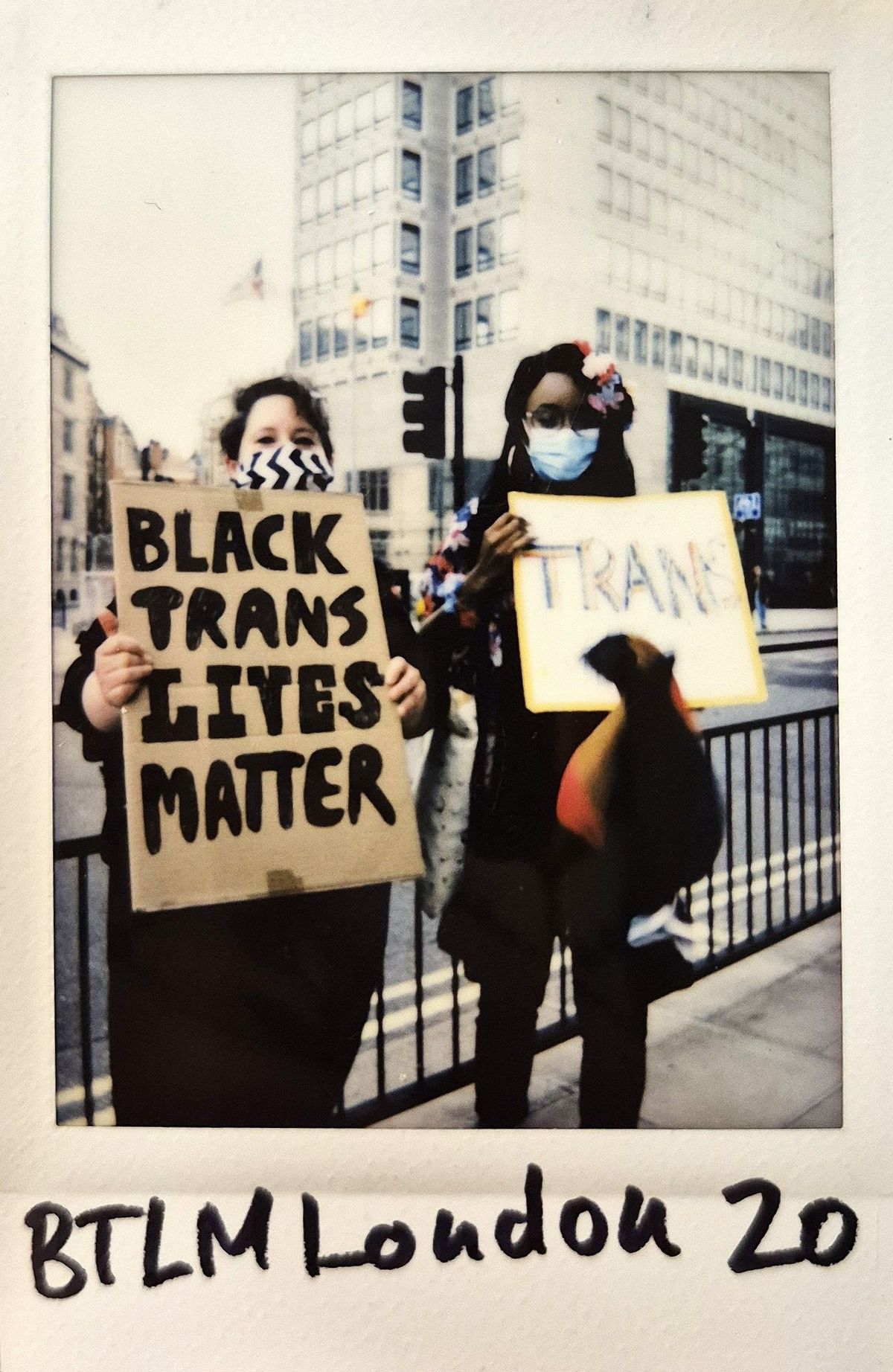 Two individuals hold signs advocating for Black trans lives during a protest on a city street.