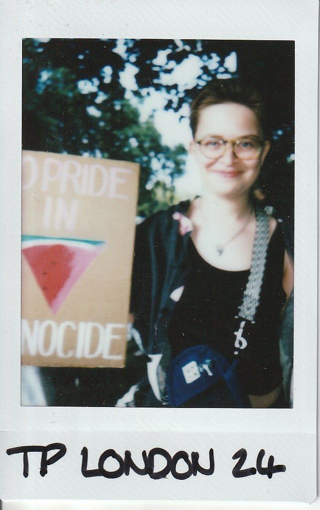 A person with glasses smiles while holding a sign with a message.