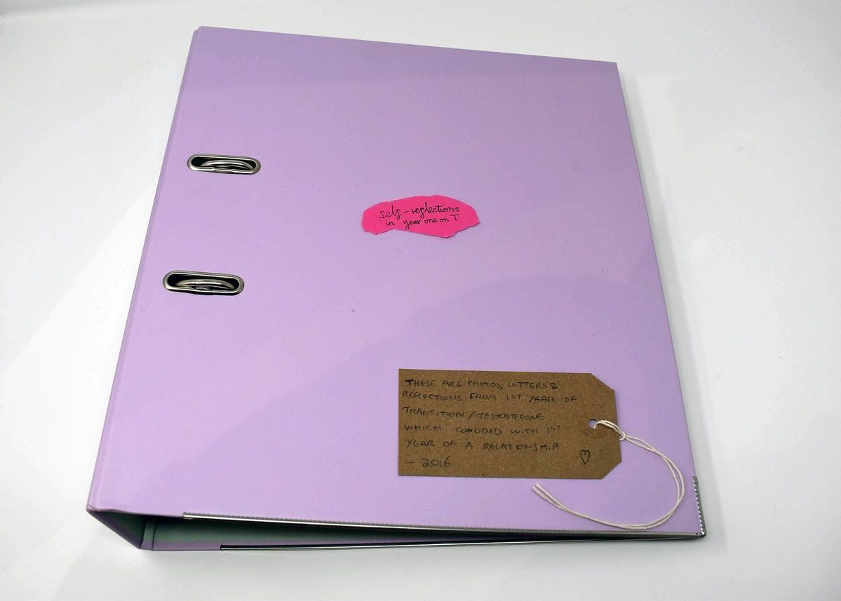 A pink folder which has a pink postit on top of it and a brown luggage tag with writing on it.