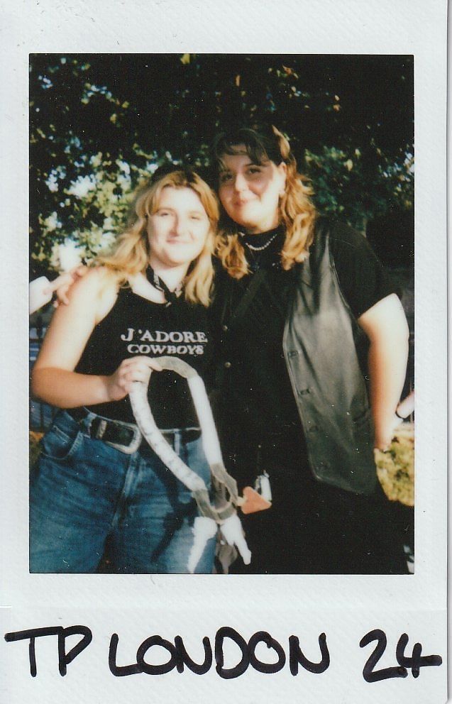 Two people smile together outdoors; one wears a "J'adore Cowboys" shirt, the other a leather vest.
