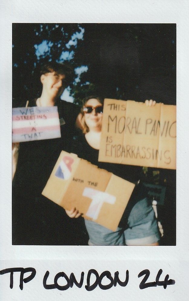 Two people hold signs expressing opinions on a controversial topic, standing outdoors with trees in the background.