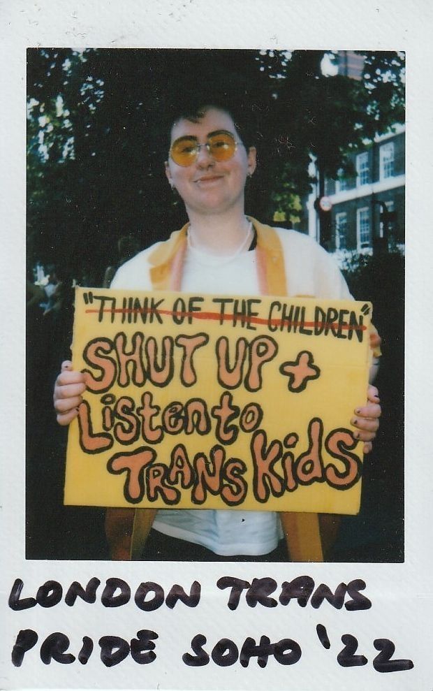 A person holds a sign reading "Shut Up & Listen to Trans Kids" at London Trans Pride.