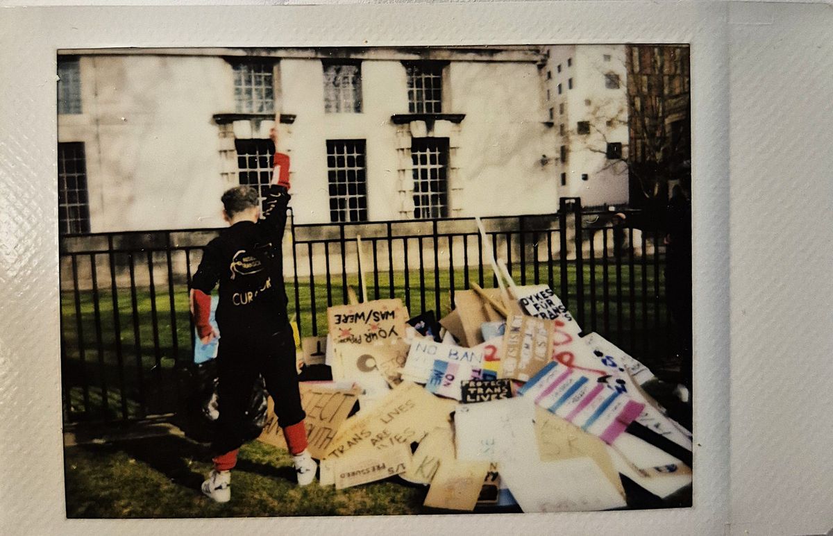 A person stands with a raised fist near a pile of protest signs outside a building.