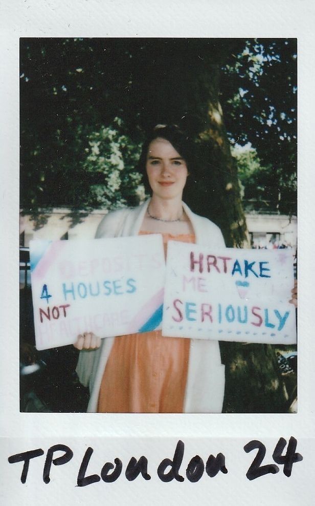 A person stands outdoors holding two signs, advocating for serious attention and housing, not just promises.