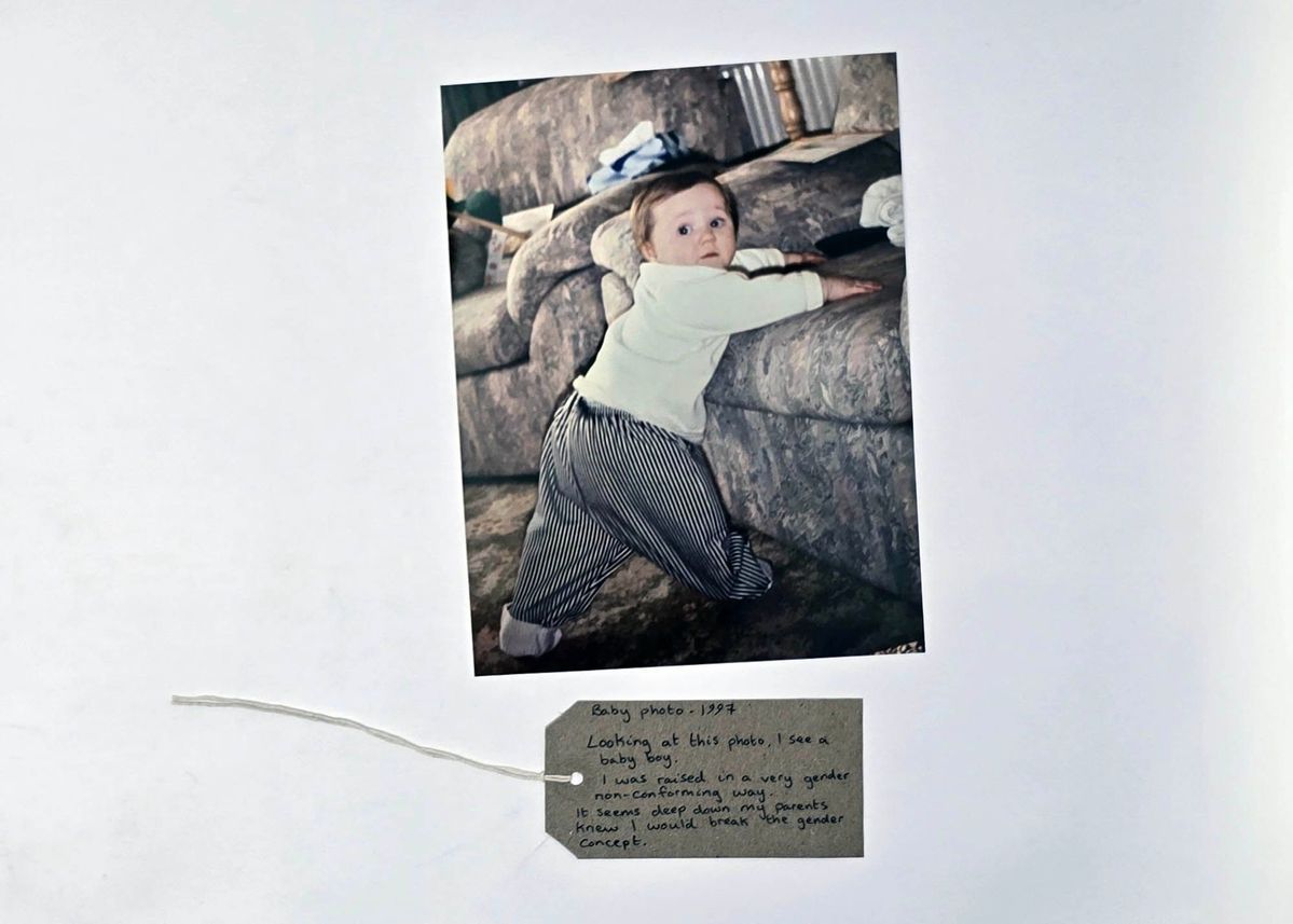 A photo of a young child with light brown hair wearing a white top and pin stripe trousers about to climb onto a sofa. With a brown handwritten luggage tag.