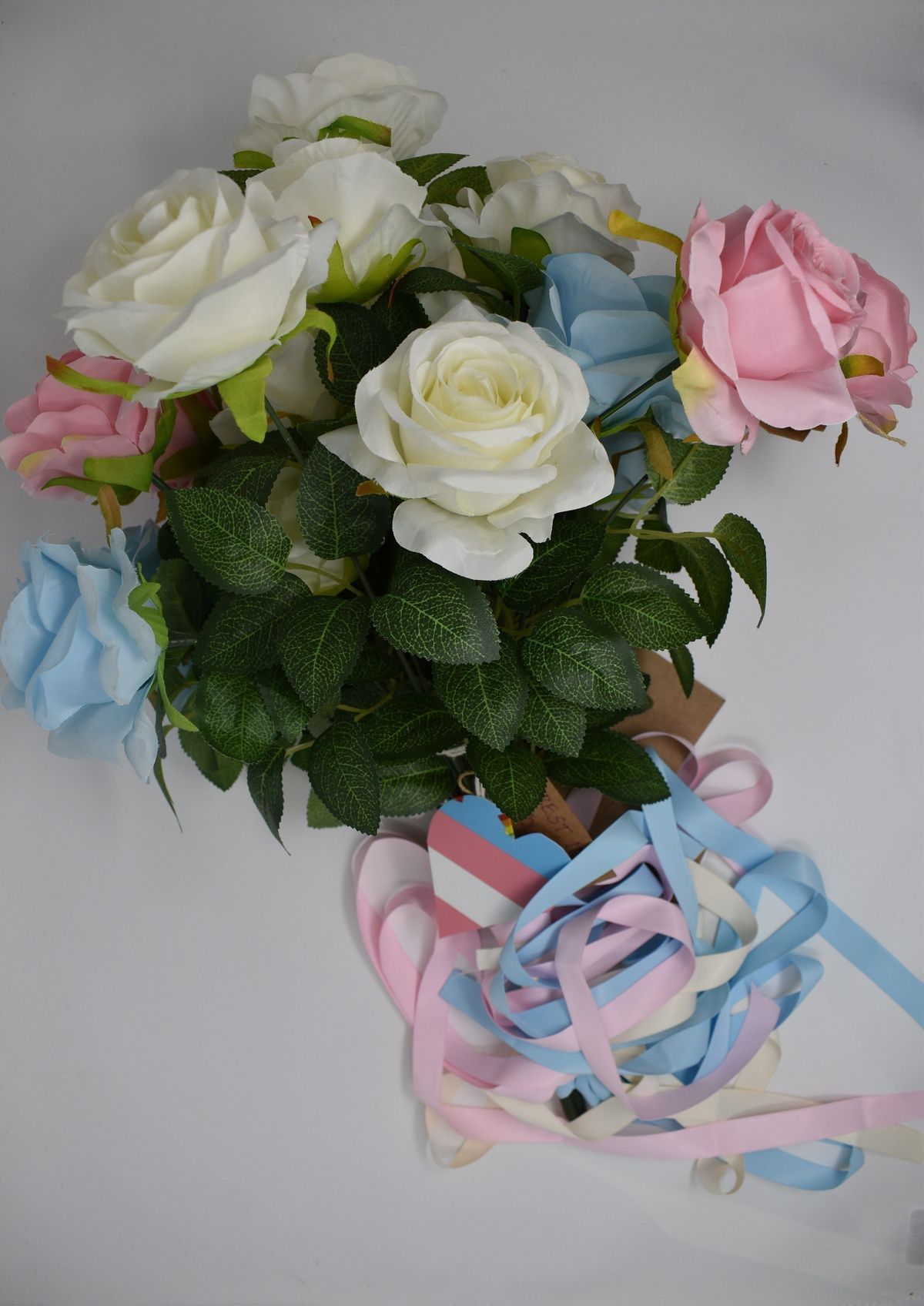 A bouquet of flowers which are fake roses in trans flag colours, tied up with the same coloured ribbons.