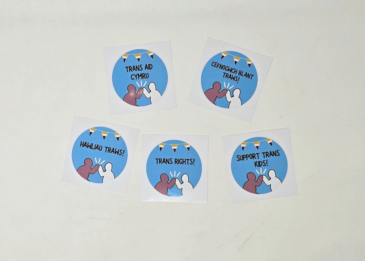 Five stickers on a white surface promote trans rights and support.