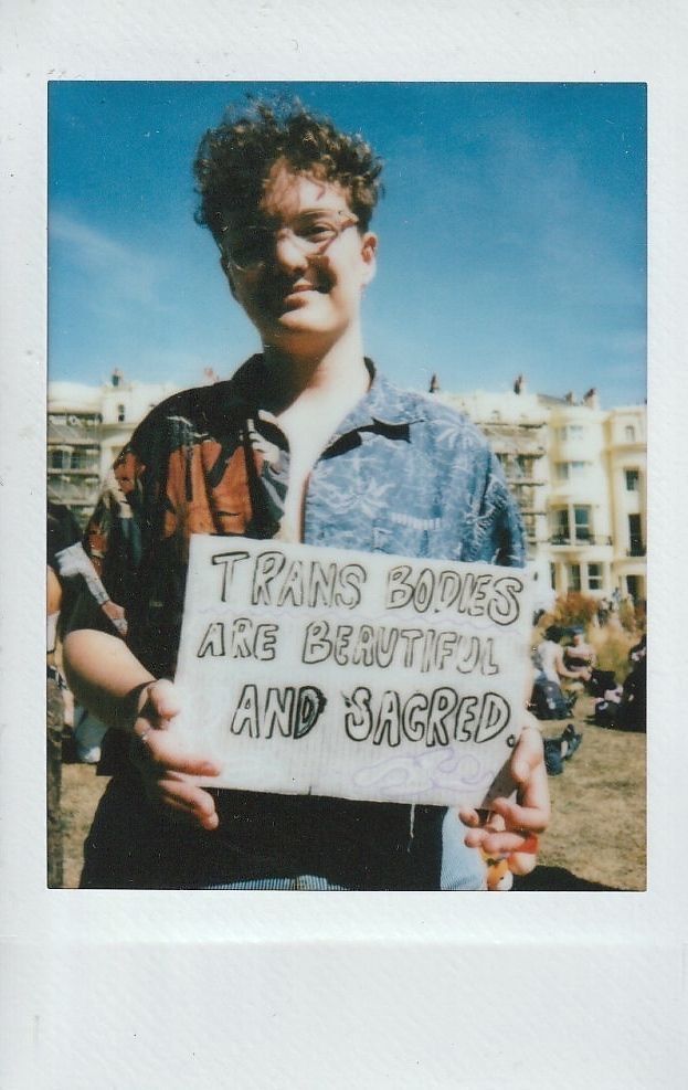A person is holding a sign that reads, "Trans bodies are beautiful and sacred".