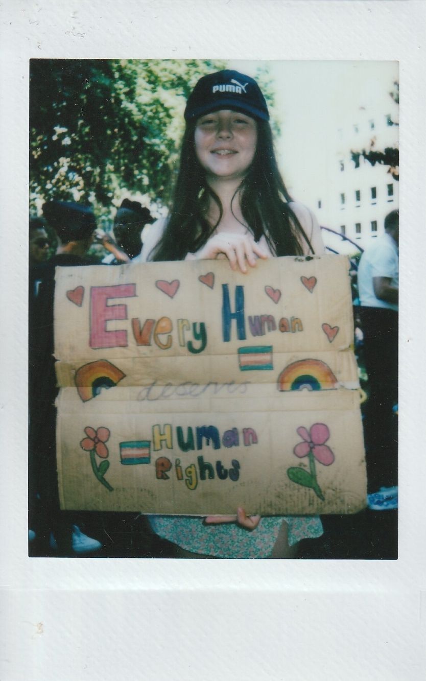 A person wearing a cap holds a colorful sign which says "Every Human Deserves Human Rights".
