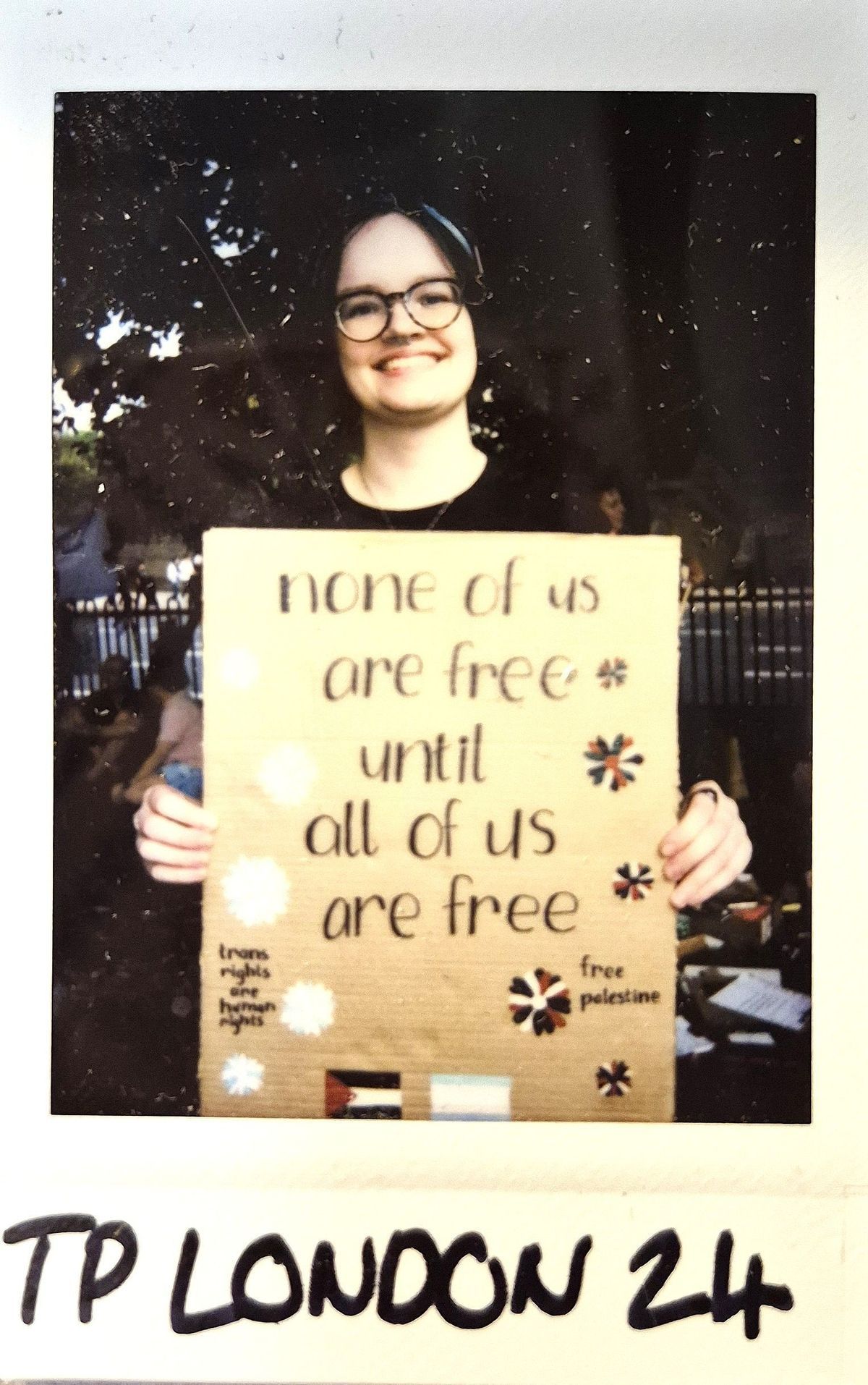 A person is smiling while holding a cardboard sign advocating freedom and equality for everyone.