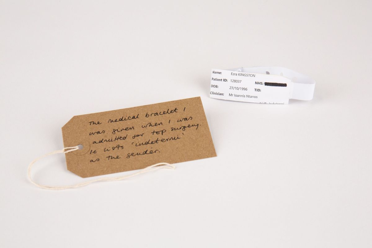 A white hospital medical bracelet. With a brown, handwritten luggage tag.