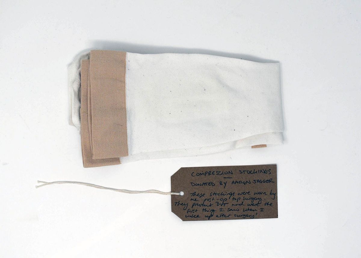 A pair of folded, beige compression stockings. With a brown, handwritten luggage tag.