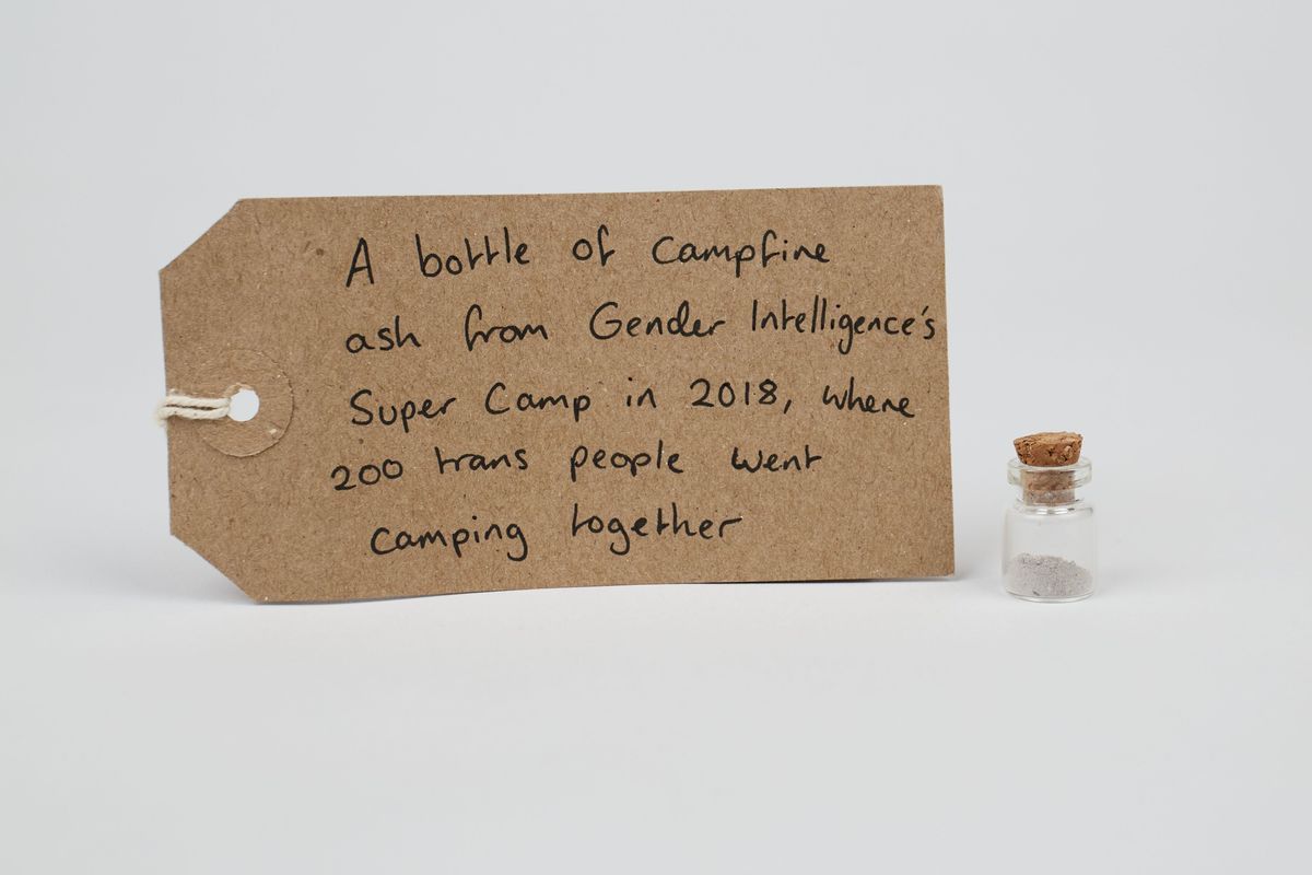 A small, corked bottle containing grey ash and a brown luggage tag.