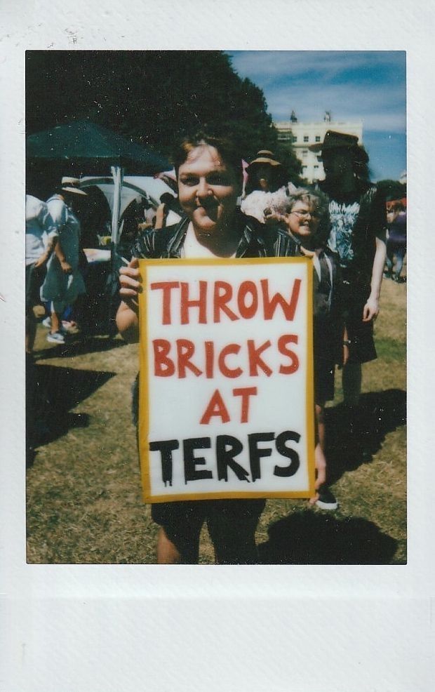 A person holds a protest sign which says "THROW BRICKS AT TERFS".