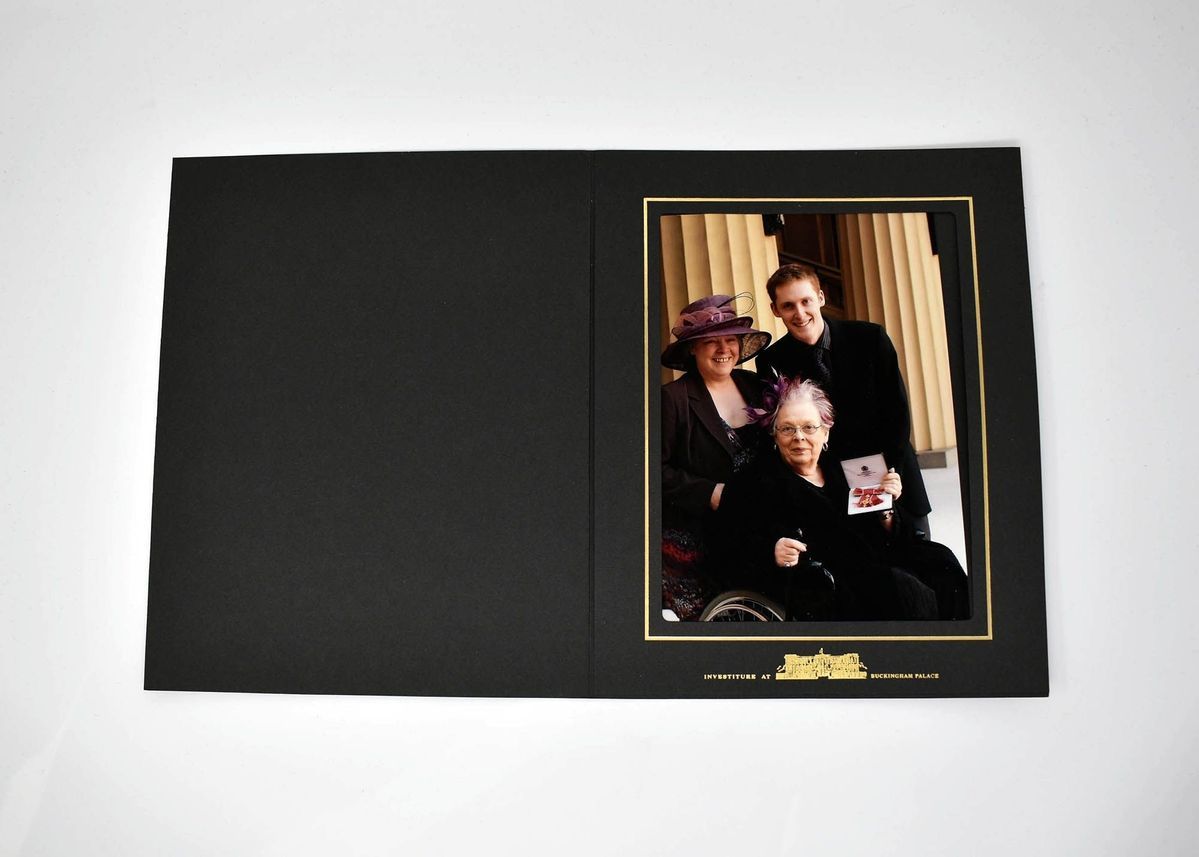 A group of three people pose together, with one holding a certificate in a framed photograph.