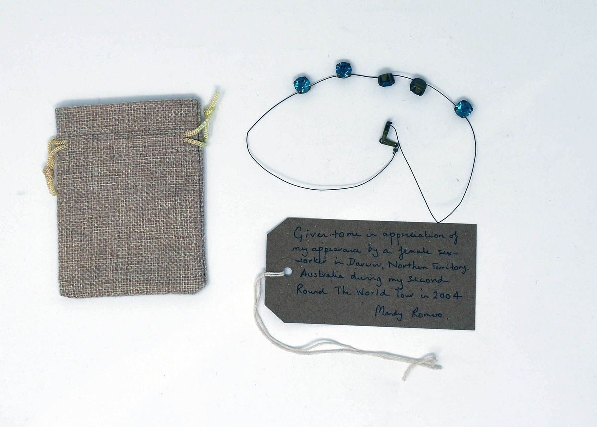 A necklace strung with 5, blue, glass, beads, a small hessian drawstring back and a brown, hand written luggage tag.