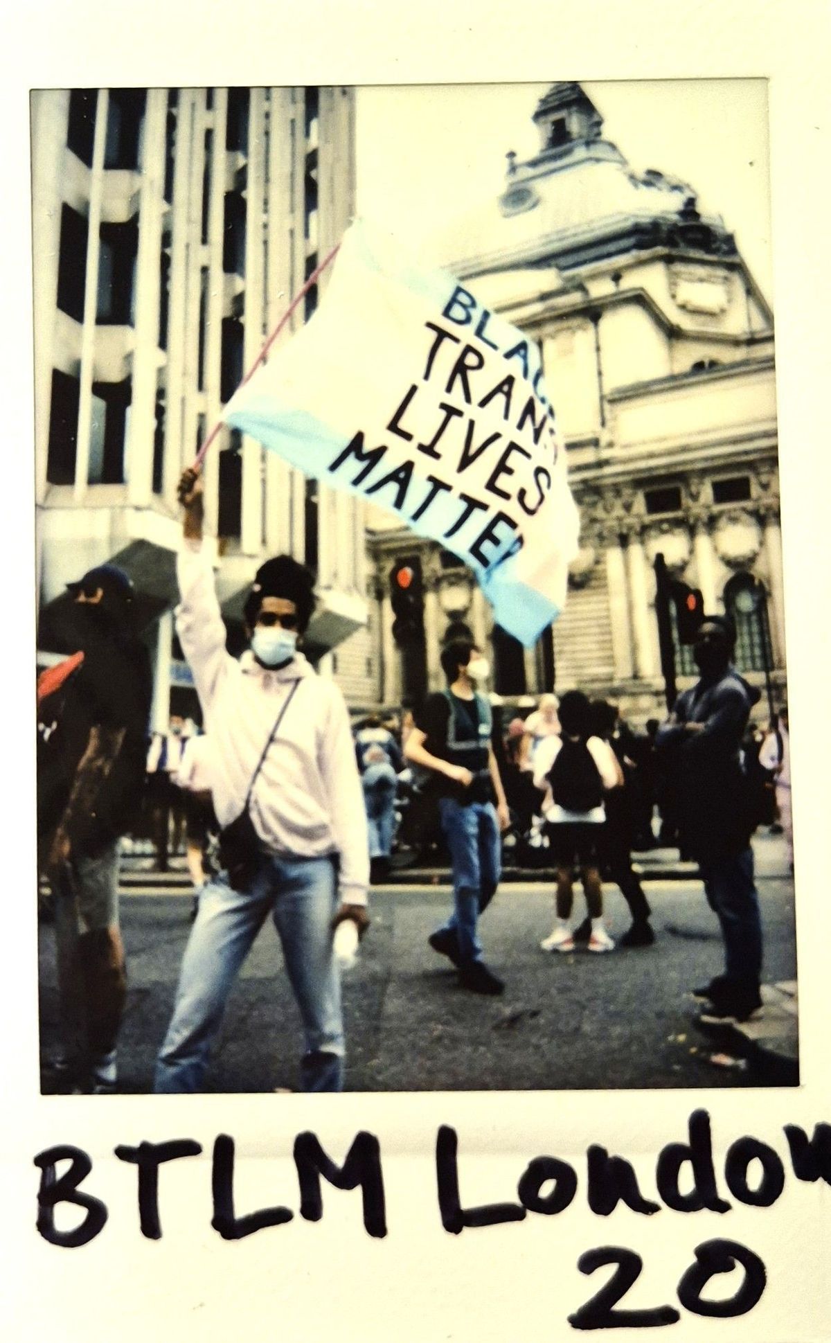 A person in a mask holds a sign that reads, "Black Trans Lives Matter" at a protest.