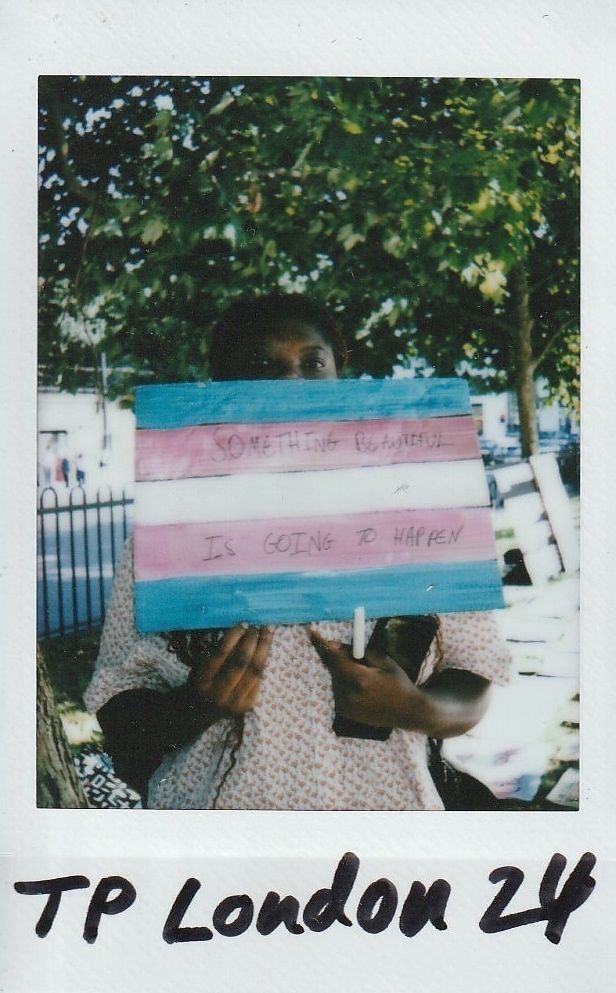 A person holds a sign with a hopeful message, standing outside near trees on a sunny day.