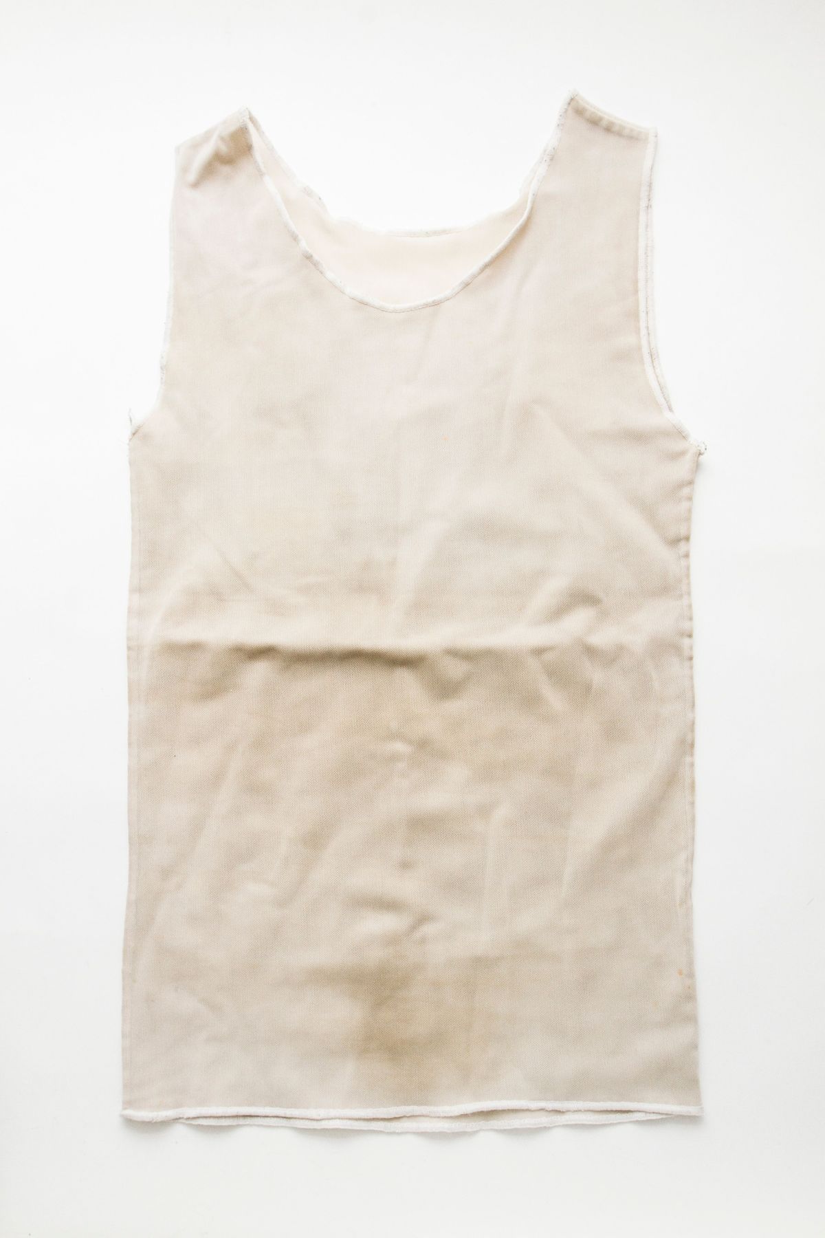 A white chest binder is laid flat on a white surface, showing its front with a light brown stain on the bottom edge.