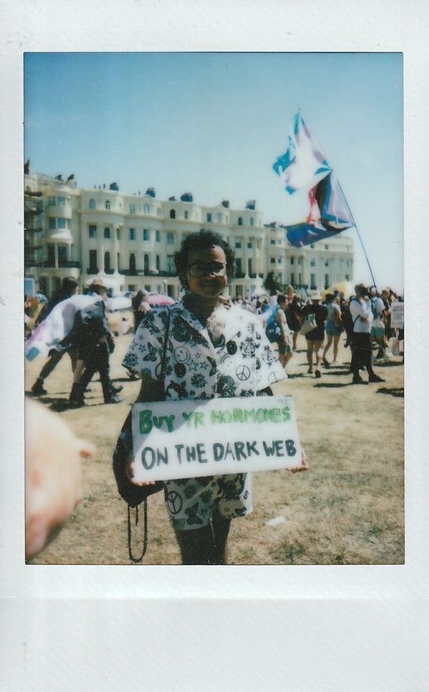 A person stands in a crowd holding a sign which says "Buy Yr Hormones On The Dark Web".