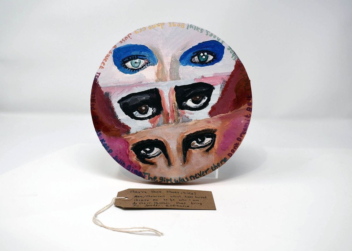 The circular artwork features three painted eye pairs with handwritten text surrounding them. With a brown handwritten luggage tag.