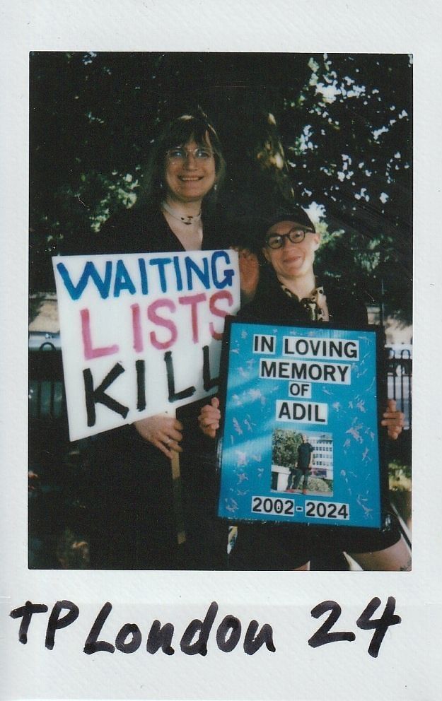 Two individuals hold signs advocating for healthcare reform, one reads "Waiting Lists Kill," urging change.
