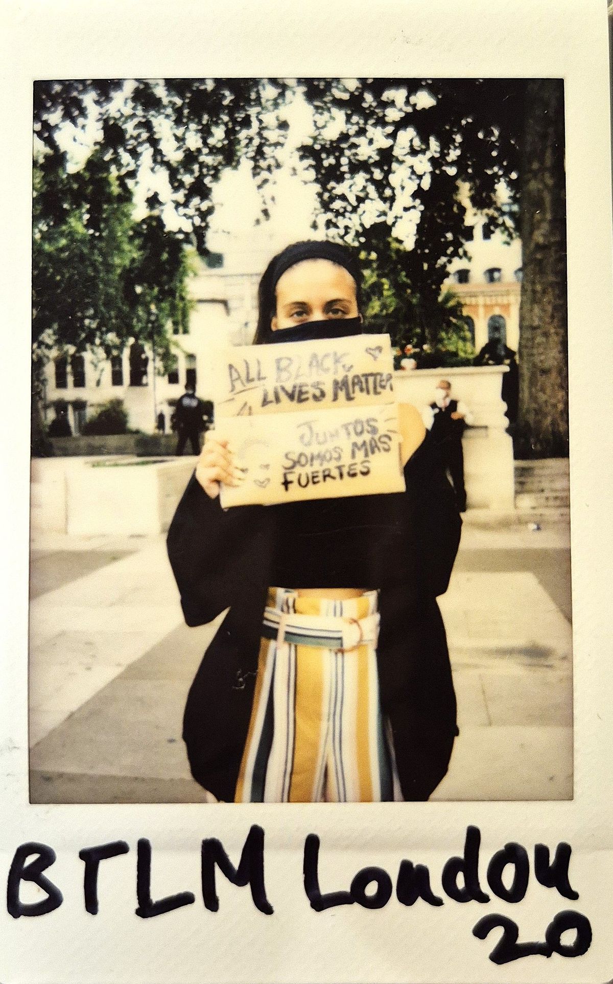 A person holds a sign reading "All Black Lives Matter" and "Juntos Somos Más Fuertes".