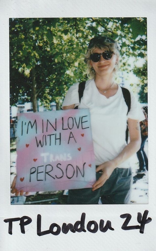 A person in sunglasses holds a sign reading "I’m in love with a trans person,".