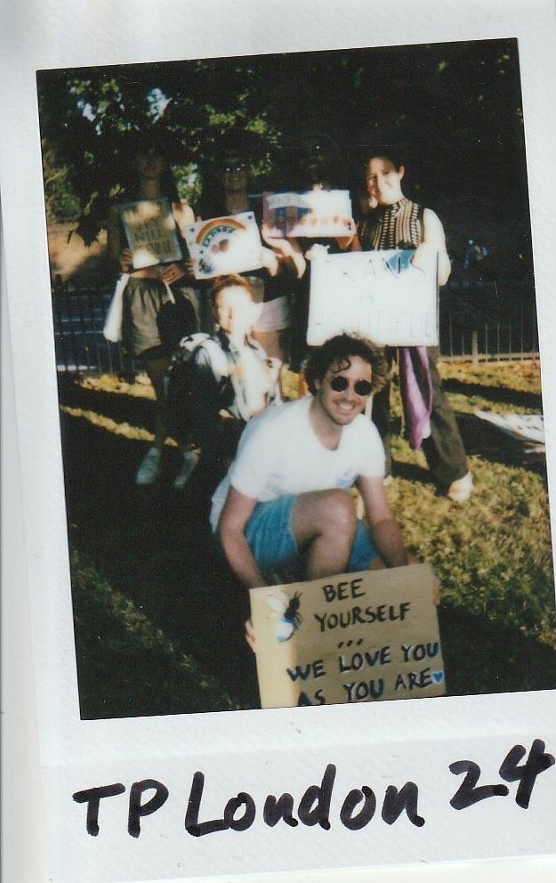 A group of people are holding supportive signs outdoors, promoting acceptance and love for everyone.