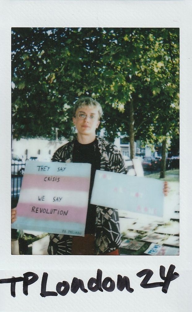 A person stands holding signs, one saying "THEY SAY CRISIS, WE SAY REVOLUTION".