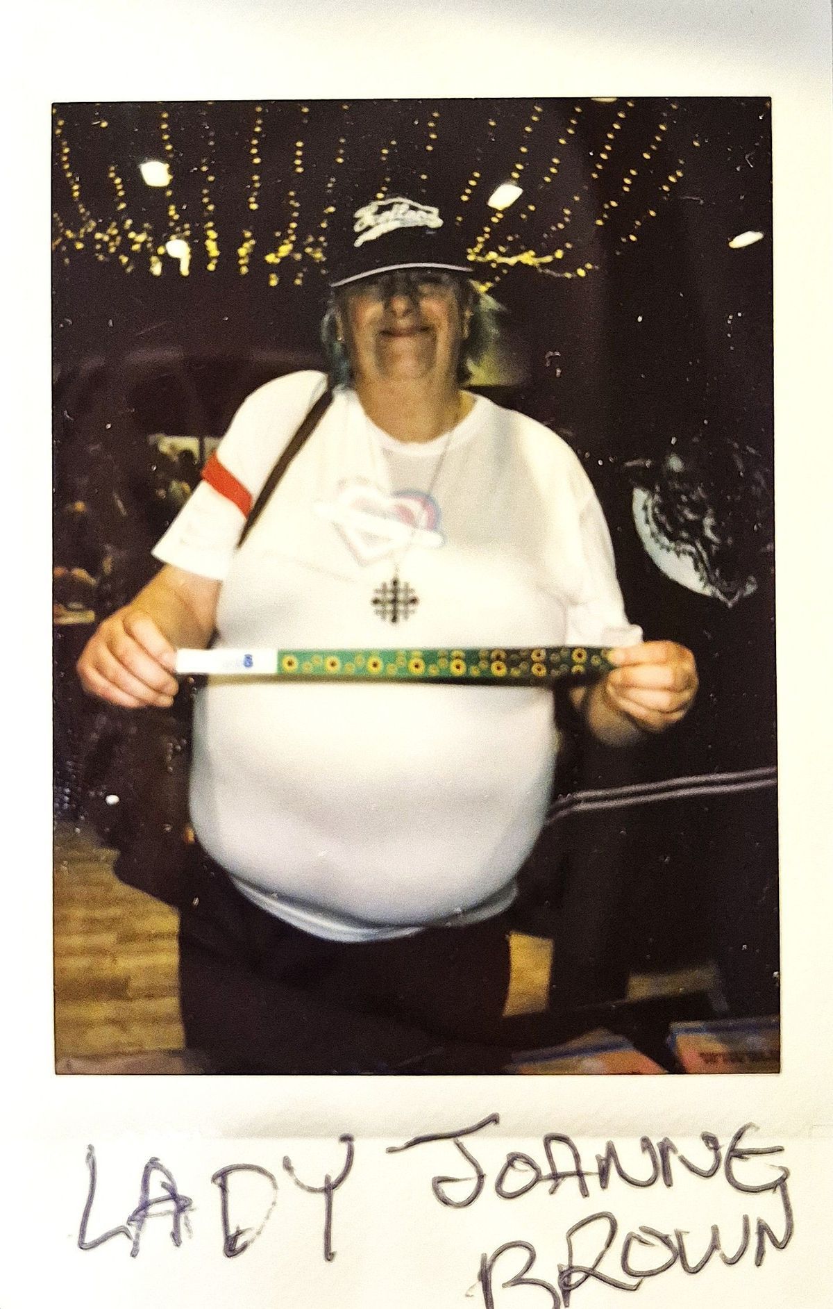 A person wearing a hat and glasses holds a decorated stick in a room with lights.