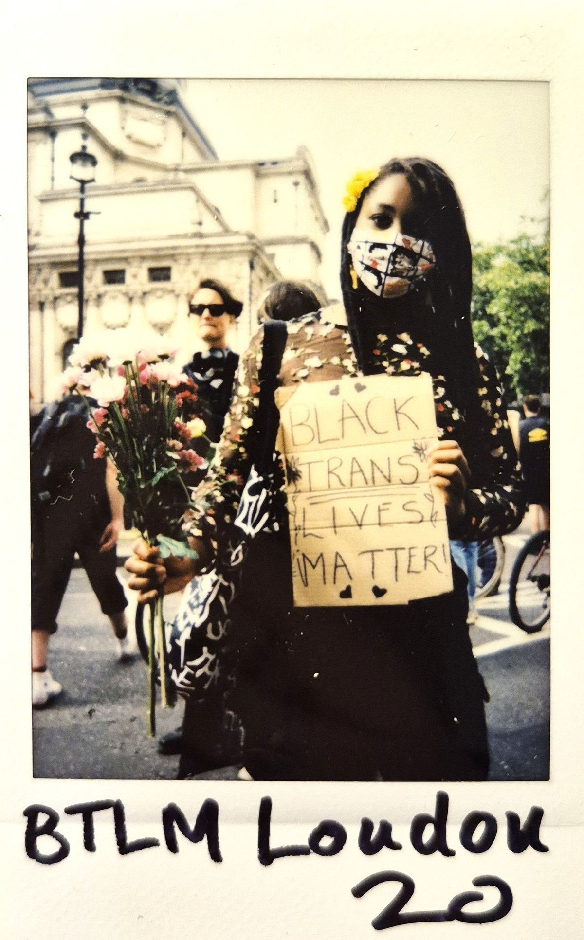 A person holds flowers and a sign reading "Black Trans Lives Matter" at a demonstration.