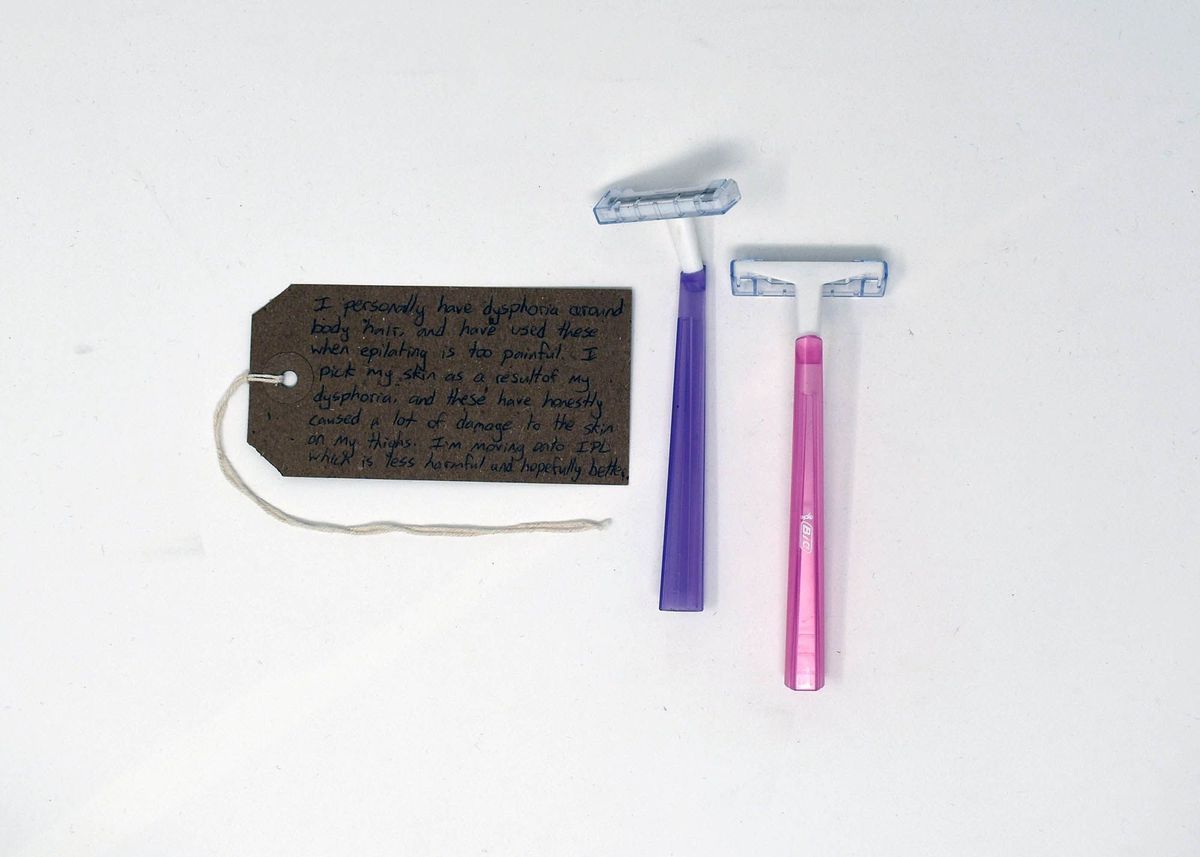 2x razors with pink and purple handles, white plastic heads and metal blade, clear plastic blade shield.