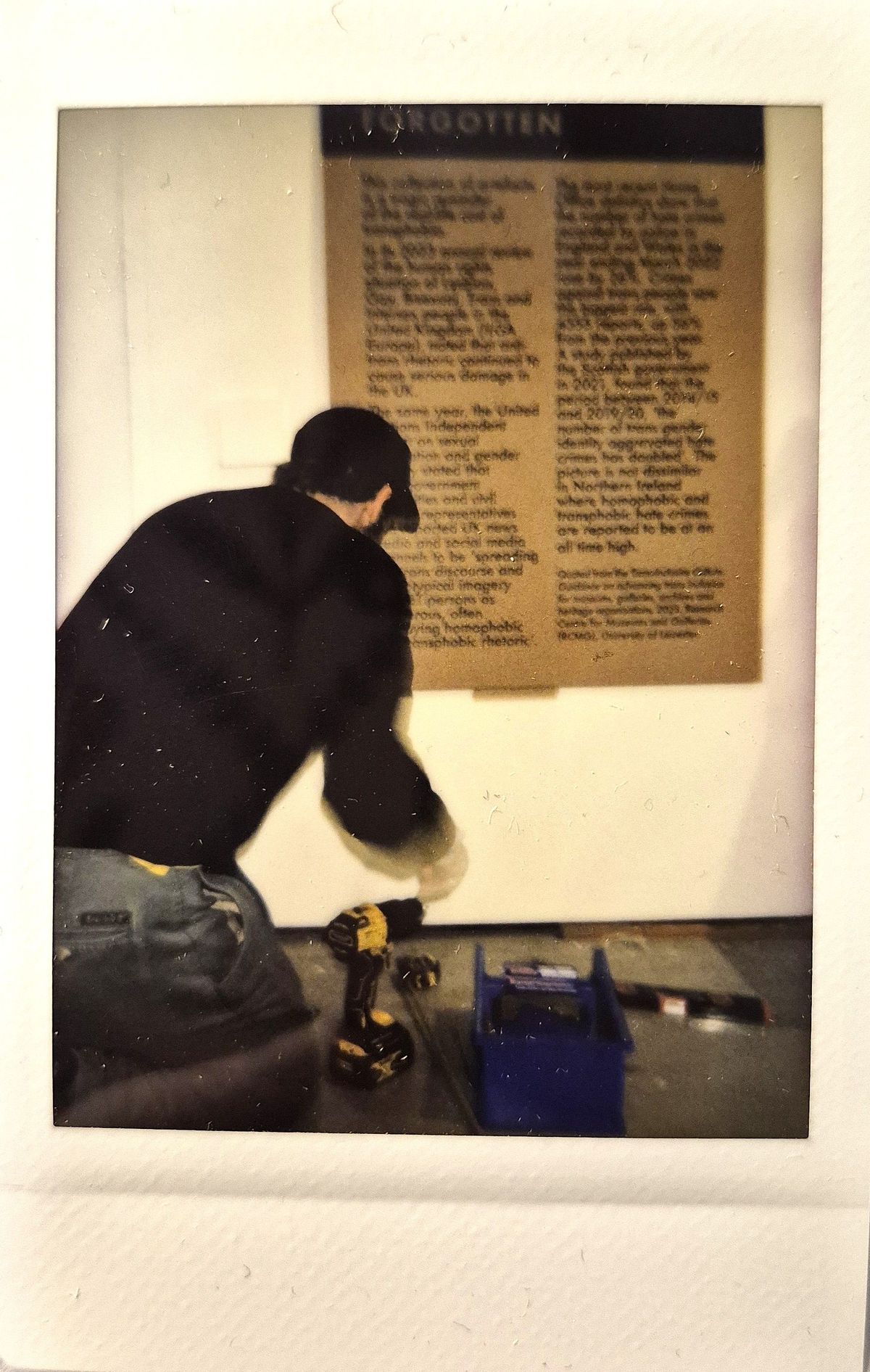 A person wearing a cap fixes something on the floor near a wall with text.