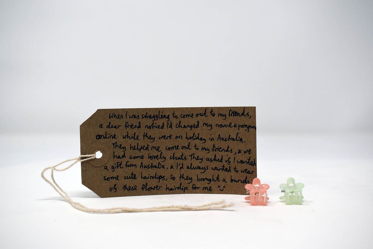 Two small flower hair clips (one orange, one green) with a brown handwritten luggage tag.