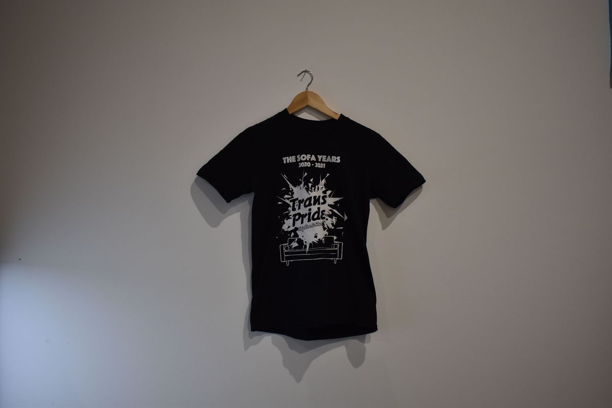A black T-shirt on a hanger displays the text design for "The Sofa Years" and "Trans Pride".