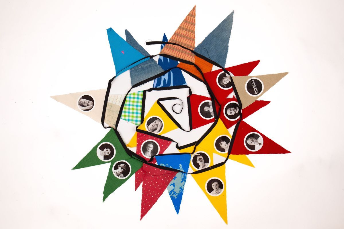 Bunting which is displayed so it is sat flat and in a spiral, overlapping. The bunting is a mixture of colours such as yellow, gree, red, blue and patterened fabric pendants. Some of the pendants have photographs of people on them.