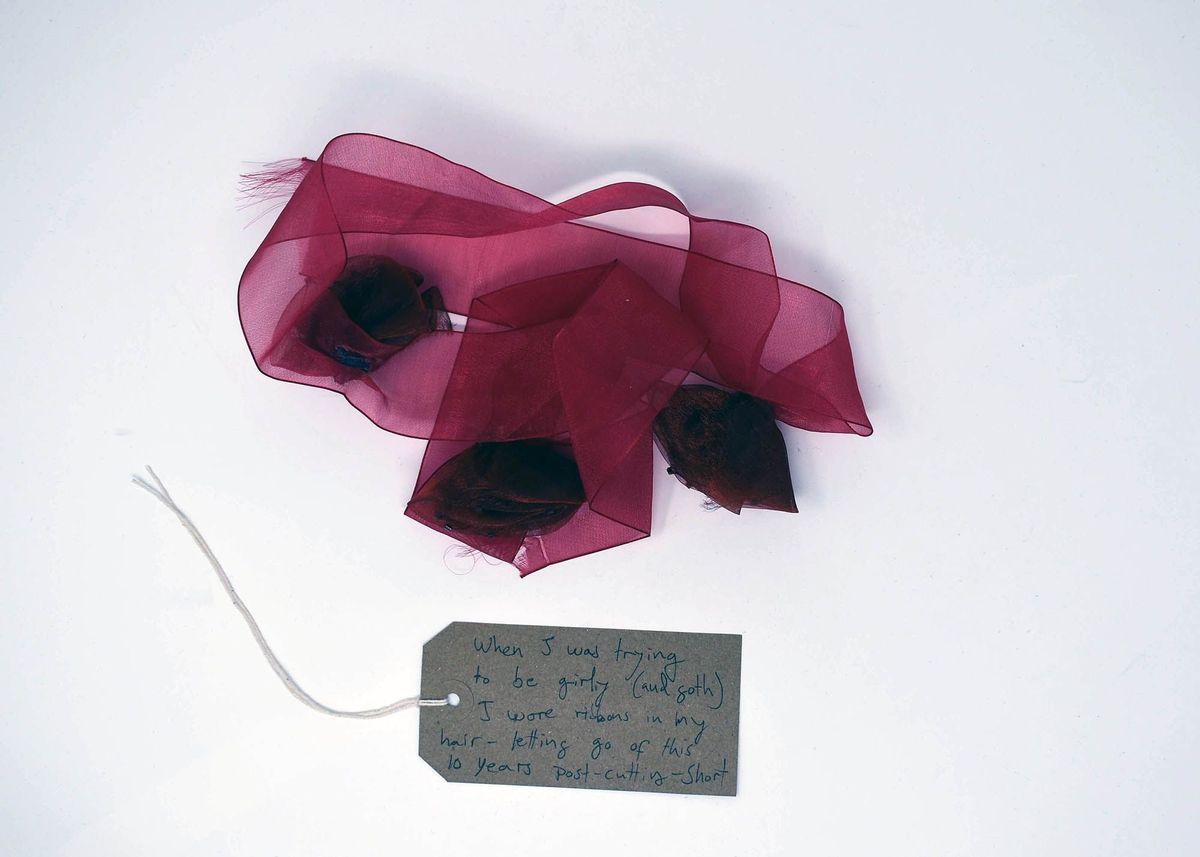 A sheer, red ribbon decorate ed with three red flowers. With a brown, handwritten luggage tag.