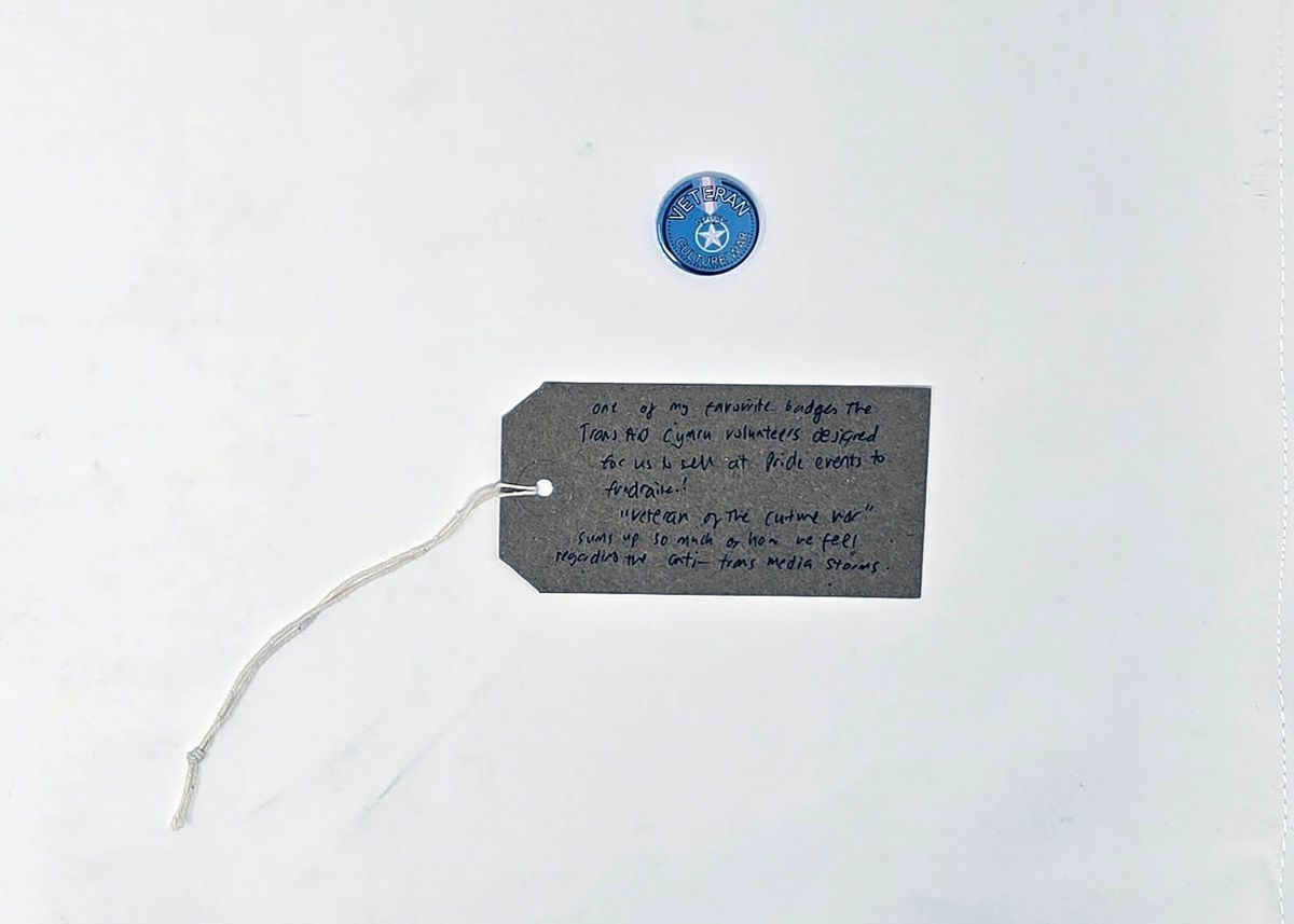 Blue pin badge inscribed "VETERAN OF THE CULTURE WAR" around a white 5 pointed star in a circle. With a brown handwritten luggage tag.