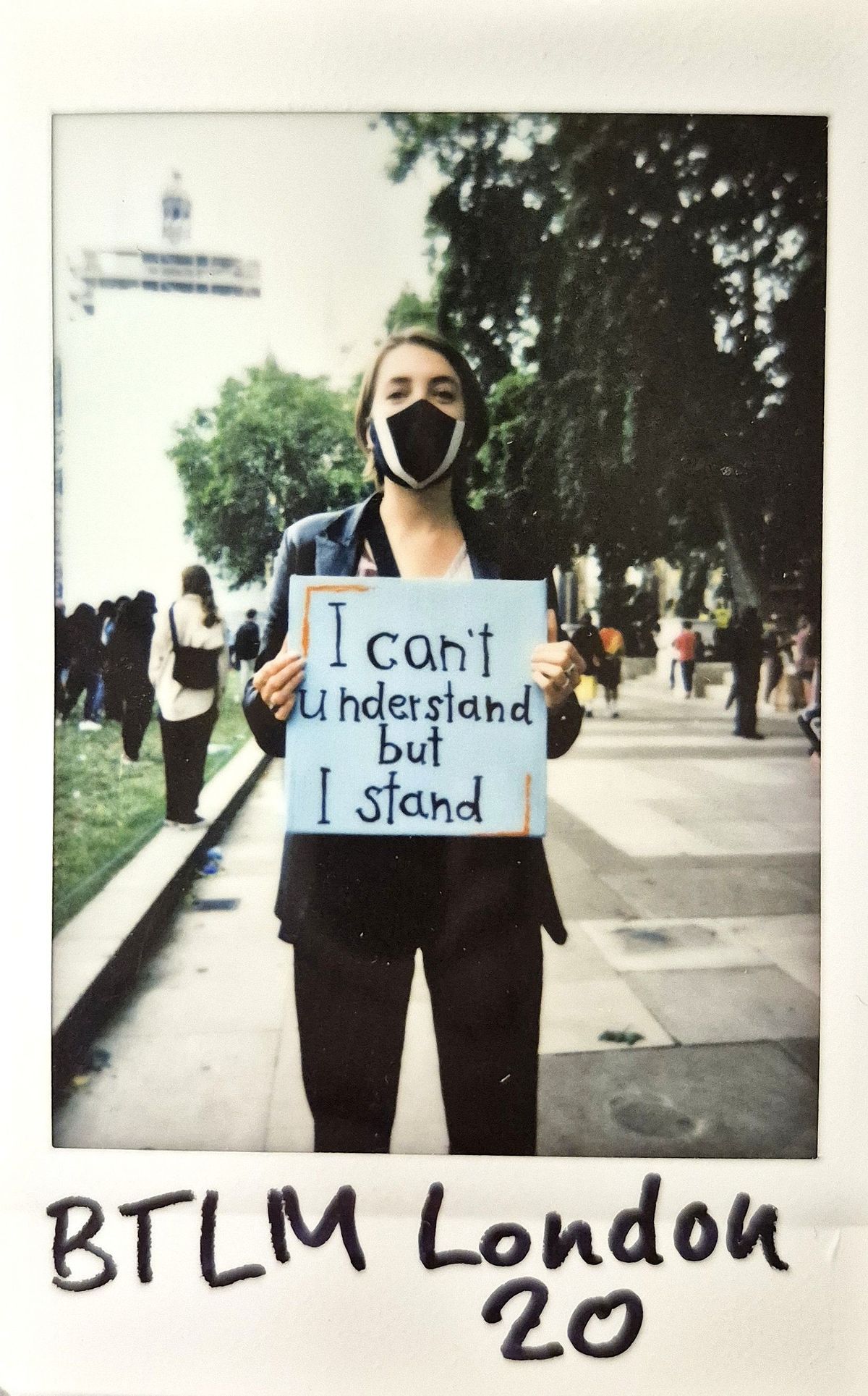 A person wearing a mask holds a sign reading "I can't understand but I stand" during a protest.