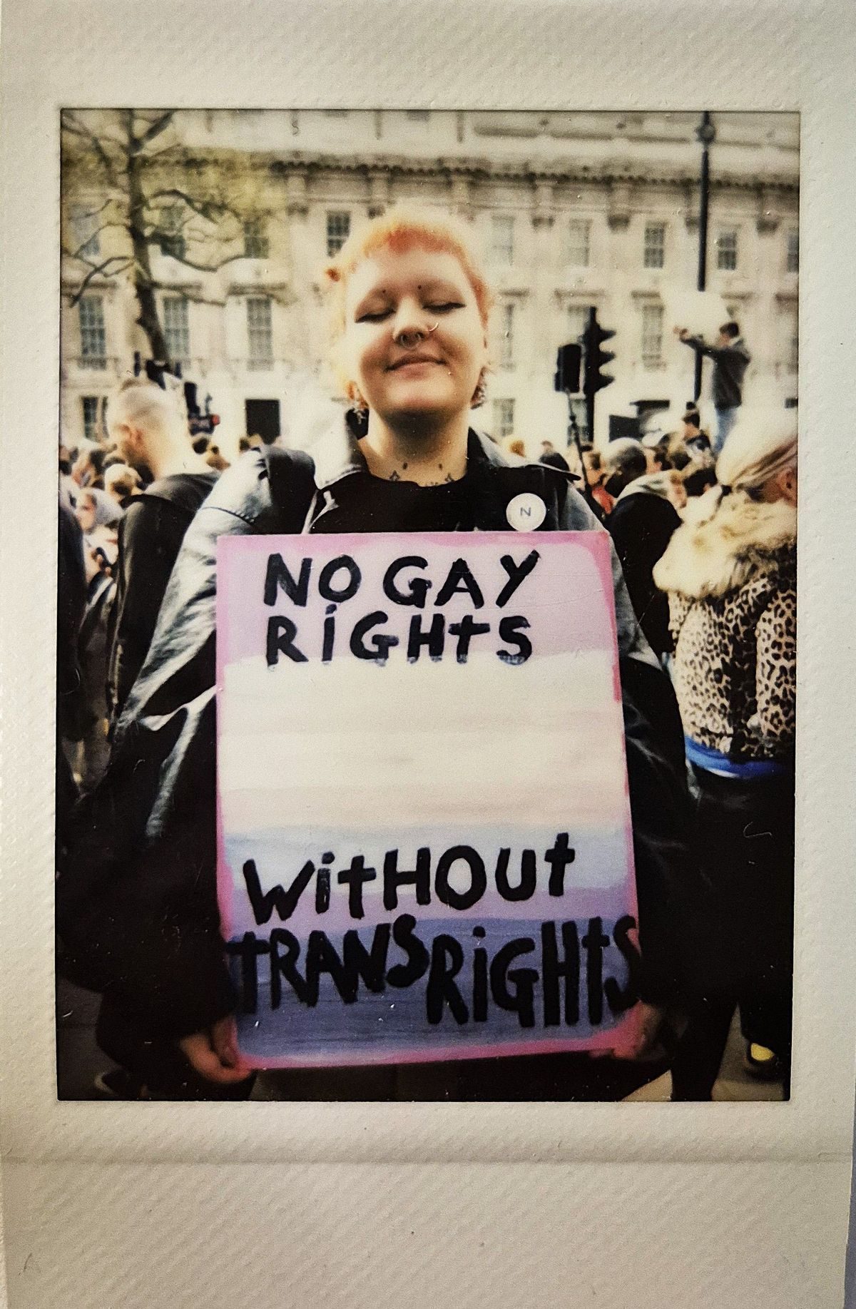 A person holds a colorful sign reading "No gay rights without trans rights" at a protest.